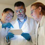 three people in lab coats looking at a tablet